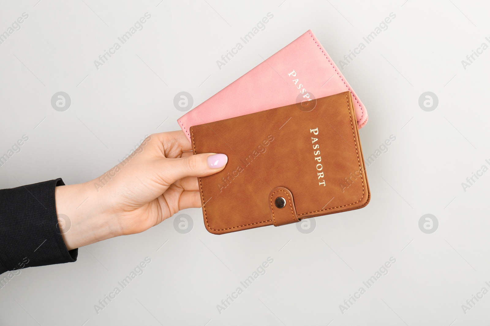 Photo of Woman holding passports in color covers on light grey background, closeup