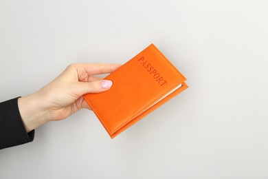 Photo of Woman holding passport in orange cover on light grey background, closeup