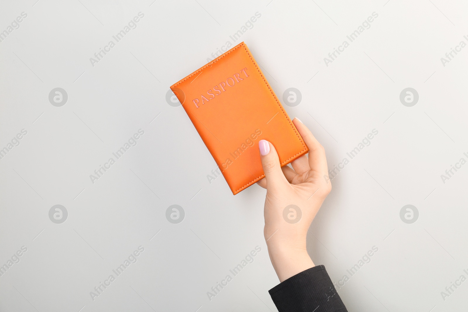 Photo of Woman holding passport in orange cover on light grey background, closeup