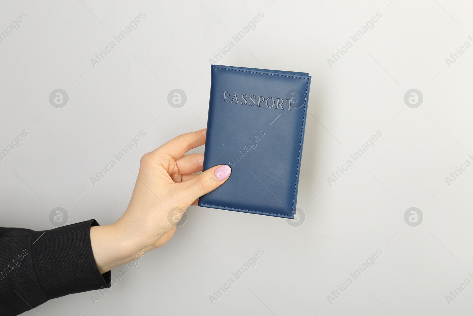 Photo of Woman holding passport in dark blue cover on light grey background, closeup