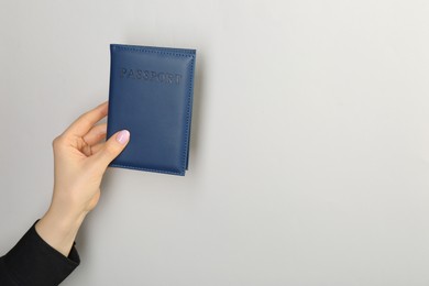 Photo of Woman holding passport in dark blue cover on light grey background, closeup. Space for text