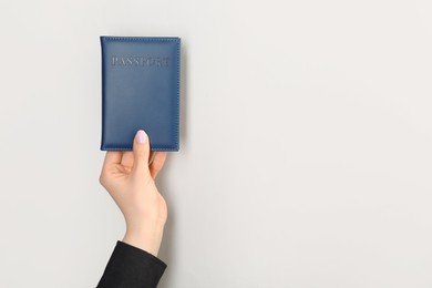 Photo of Woman holding passport in dark blue cover on light grey background, closeup. Space for text