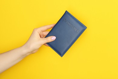 Photo of Woman holding passport in dark blue cover on yellow background, closeup