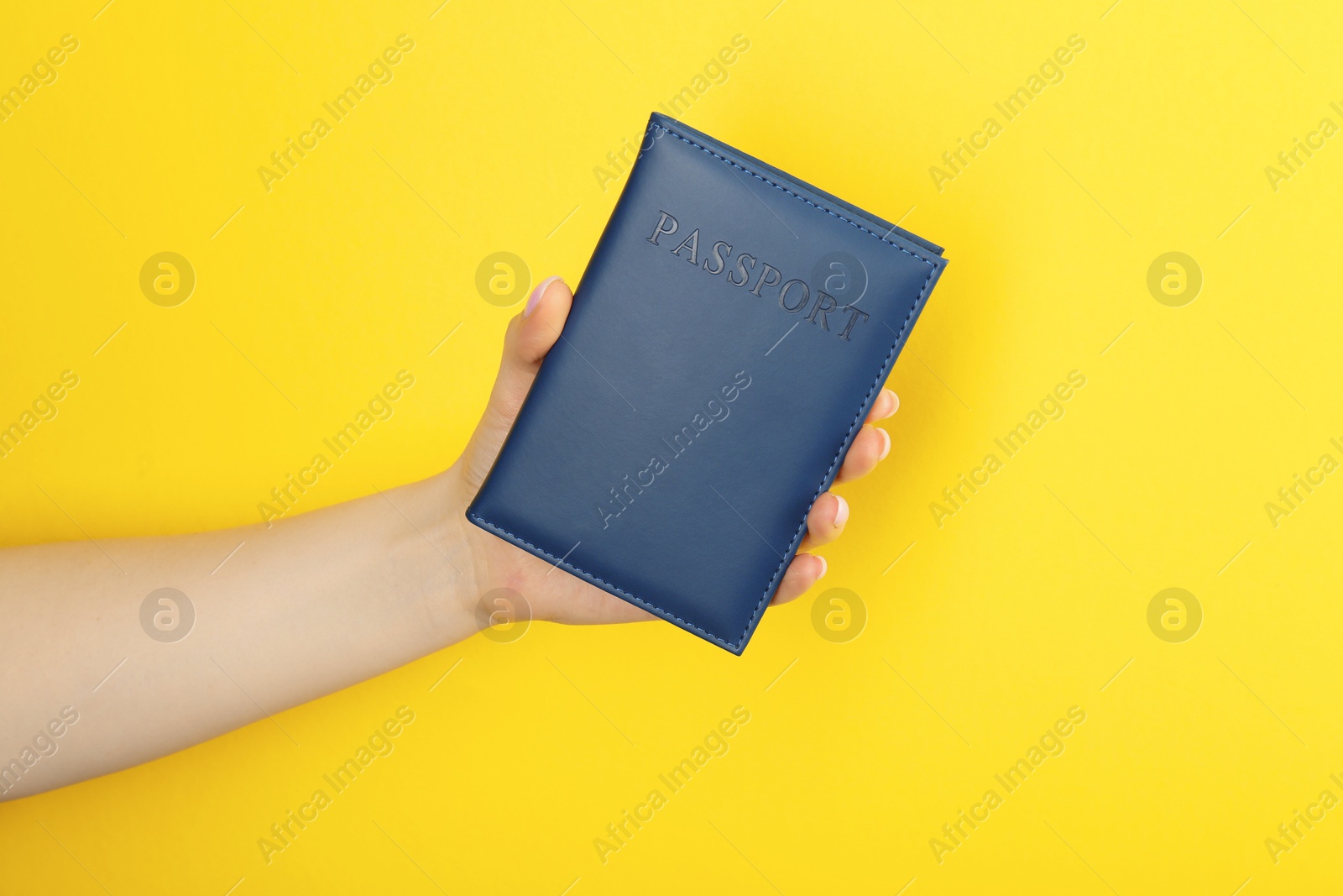 Photo of Woman holding passport in dark blue cover on yellow background, closeup