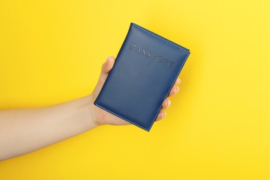 Photo of Woman holding passport in dark blue cover on yellow background, closeup