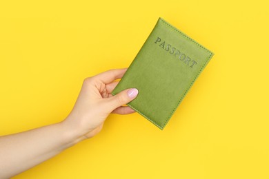 Photo of Woman holding passport in green cover on yellow background, closeup