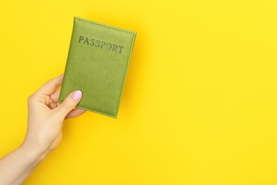 Photo of Woman holding passport in green cover on yellow background, closeup. Space for text