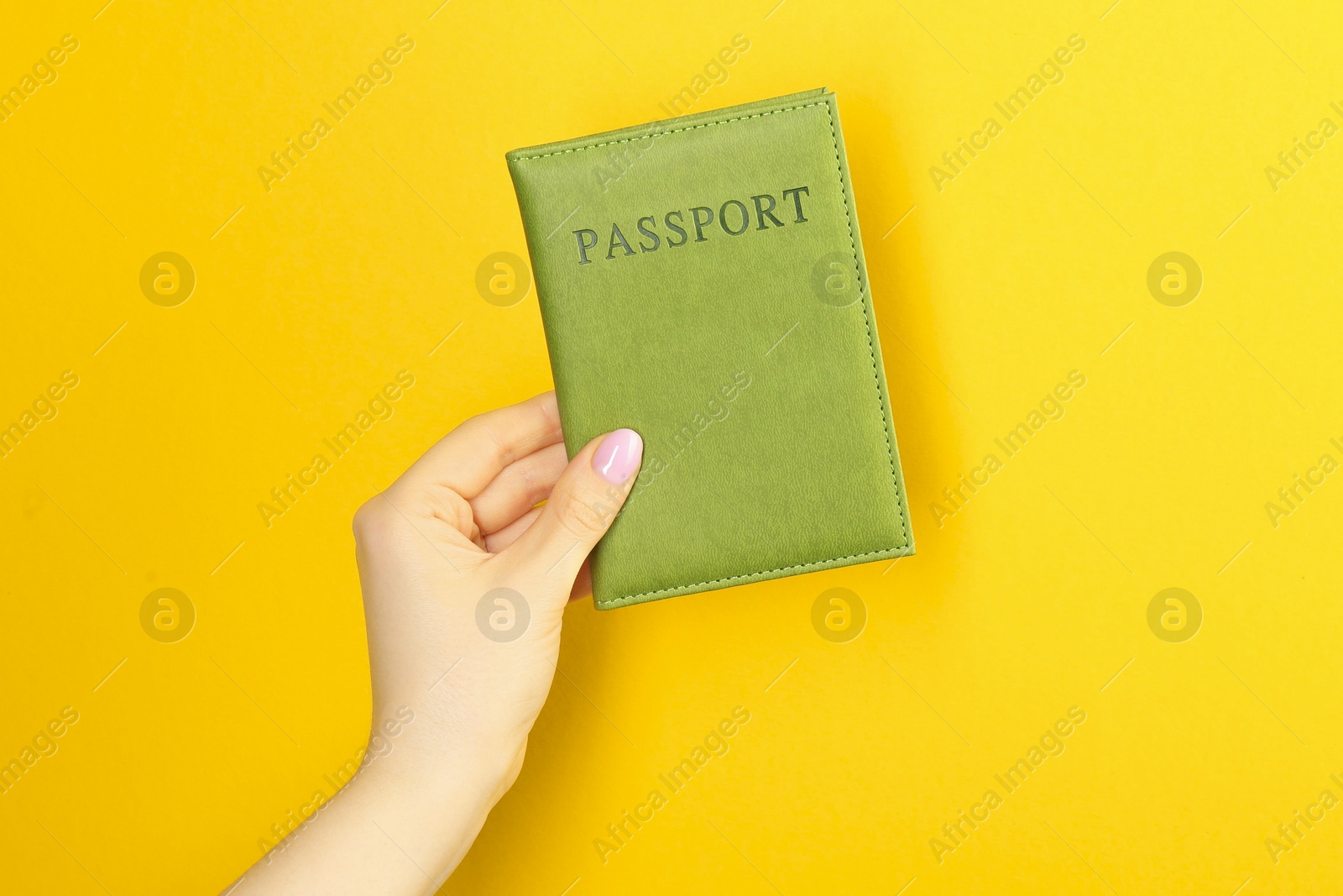 Photo of Woman holding passport in green cover on yellow background, closeup