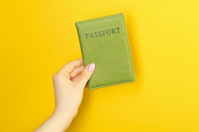 Photo of Woman holding passport in green cover on yellow background, closeup