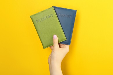 Photo of Woman holding passports in color covers on yellow background, closeup