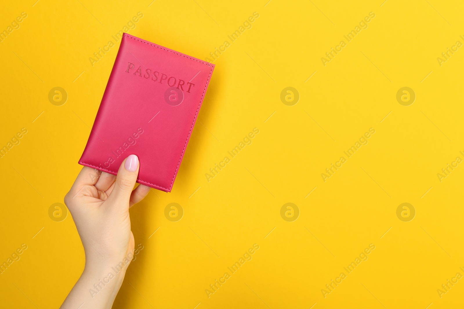 Photo of Woman holding passport in pink cover on yellow background, closeup. Space for text