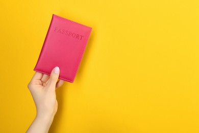 Photo of Woman holding passport in pink cover on yellow background, closeup. Space for text