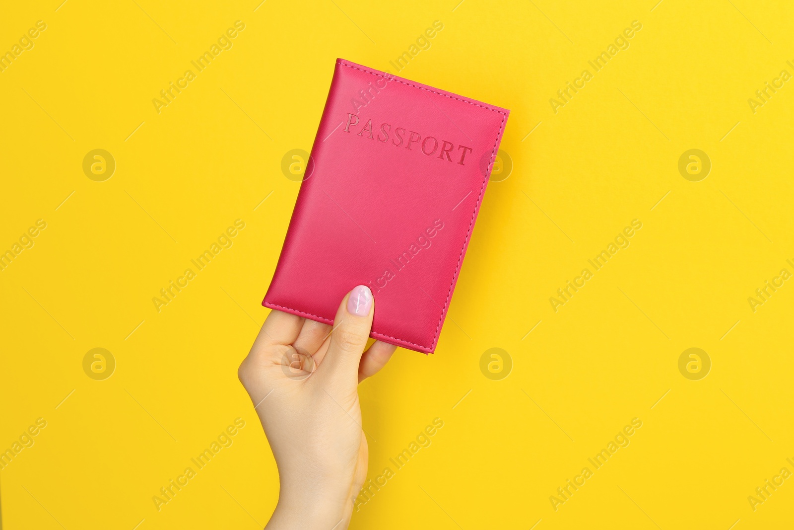 Photo of Woman holding passport in pink cover on yellow background, closeup