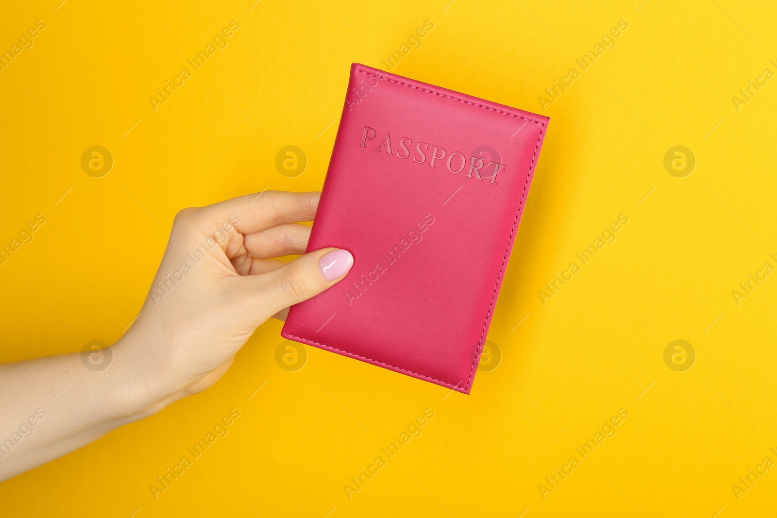 Photo of Woman holding passport in pink cover on yellow background, closeup