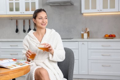 Photo of Beautiful woman pouring juice into glass after spa procedure in kitchen