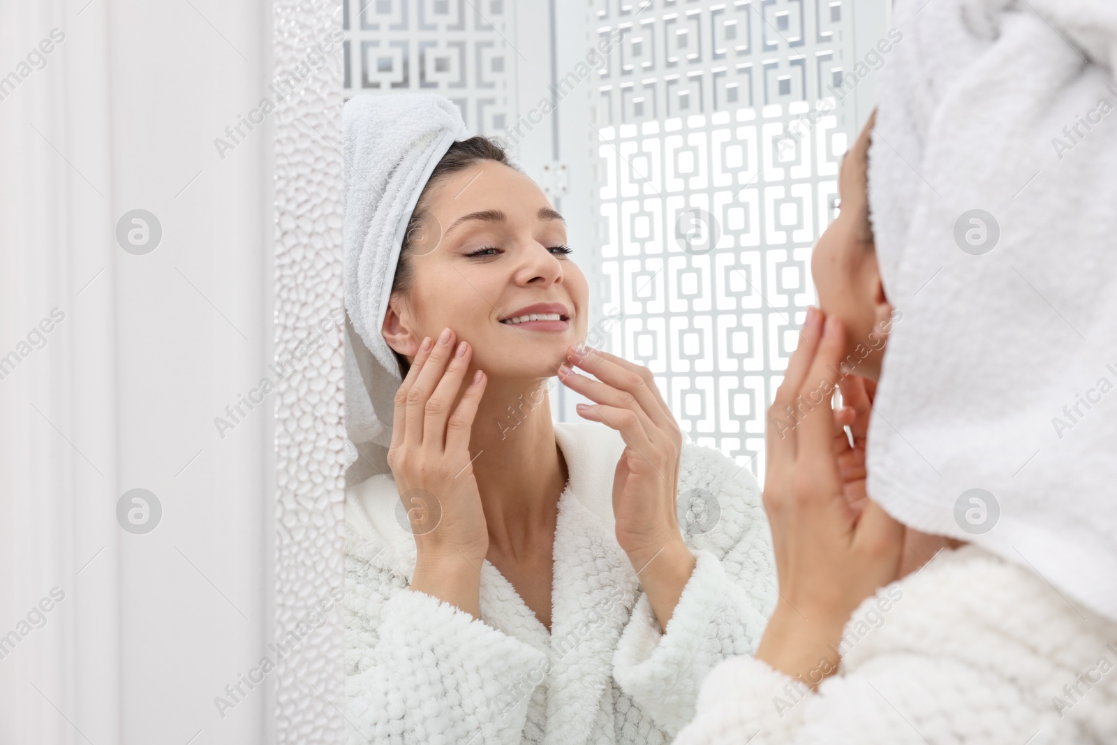 Photo of Spa day. Beautiful woman with towel on head near mirror indoors