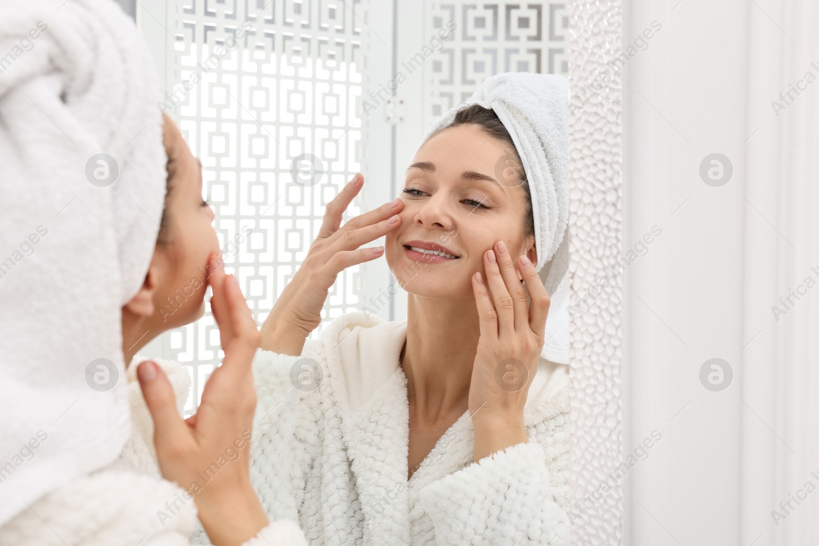 Photo of Spa day. Beautiful woman with towel on head near mirror indoors