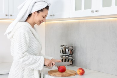 Photo of Beautiful woman cutting apple after spa procedure in kitchen