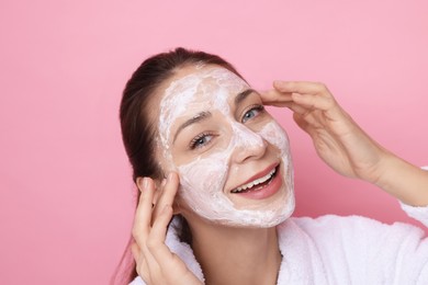 Photo of Spa day. Beautiful woman applying mask onto her face on pink background