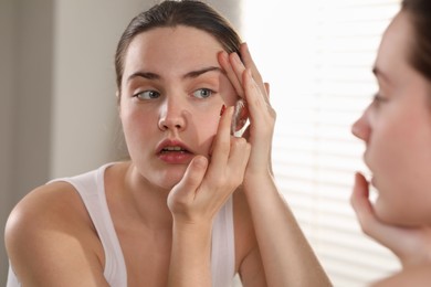 Photo of Young woman putting in red color contact lens near mirror indoors