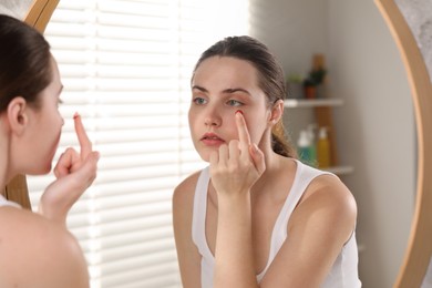 Photo of Young woman putting in red color contact lens near mirror indoors