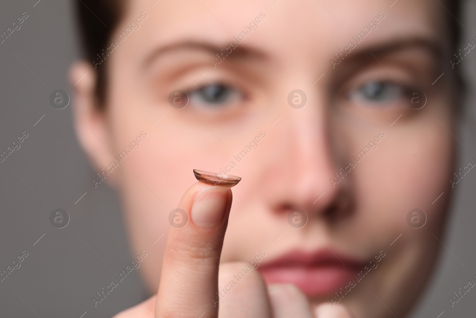 Photo of Woman with color contact lens on grey background, closeup. Selective focus