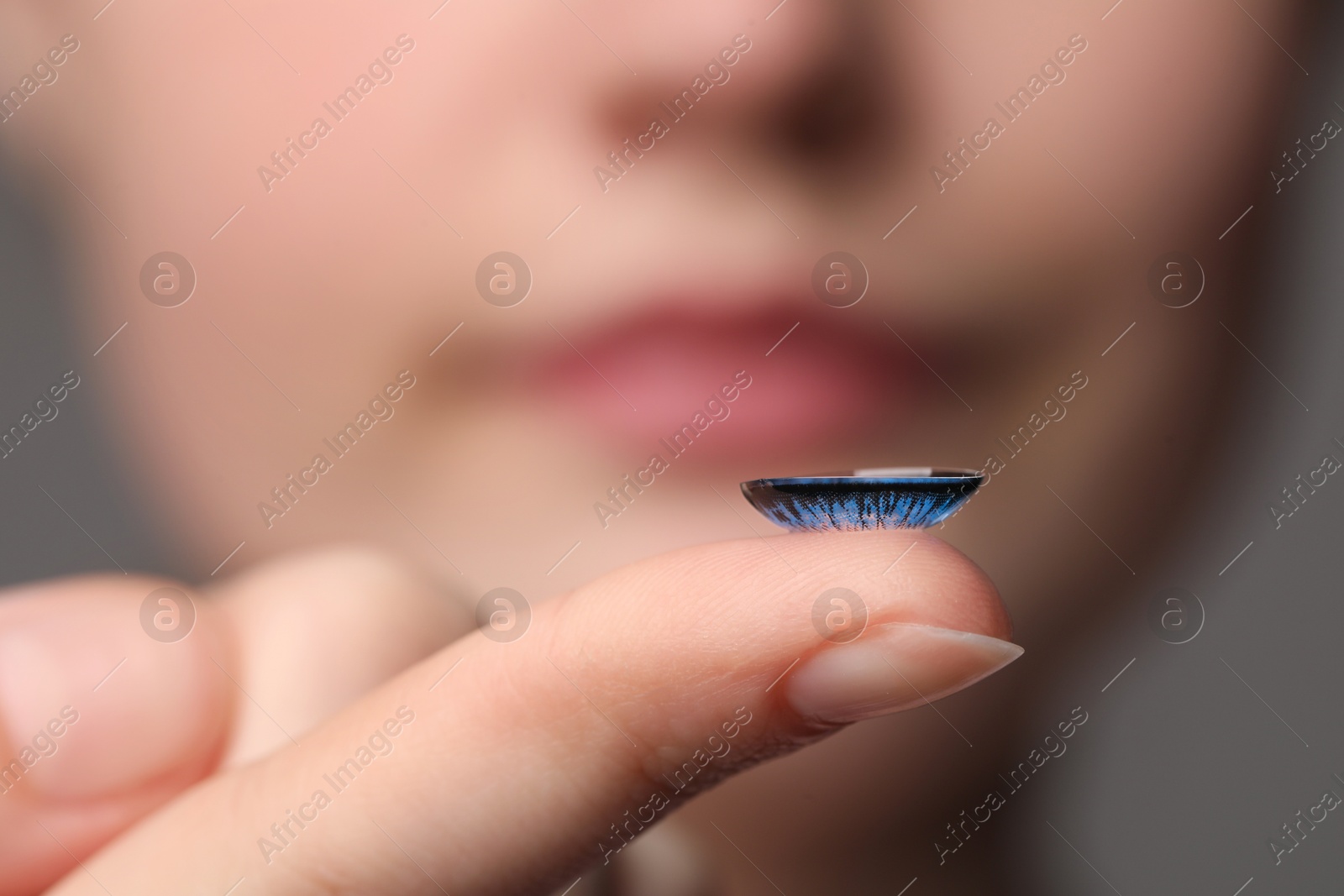 Photo of Woman with blue color contact lens on grey background, closeup. Selective focus