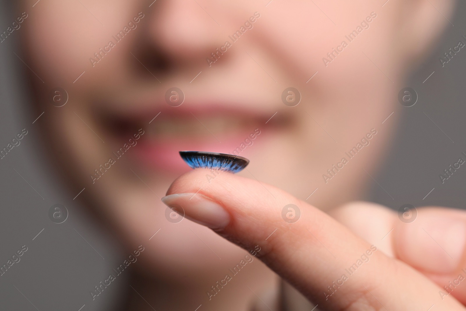 Photo of Woman with blue color contact lens on grey background, closeup. Selective focus