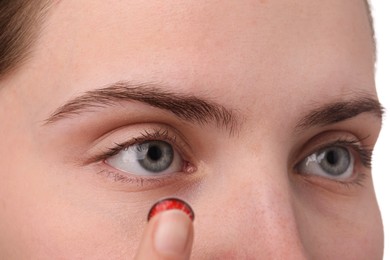 Photo of Woman putting in red color contact lens on white background, closeup