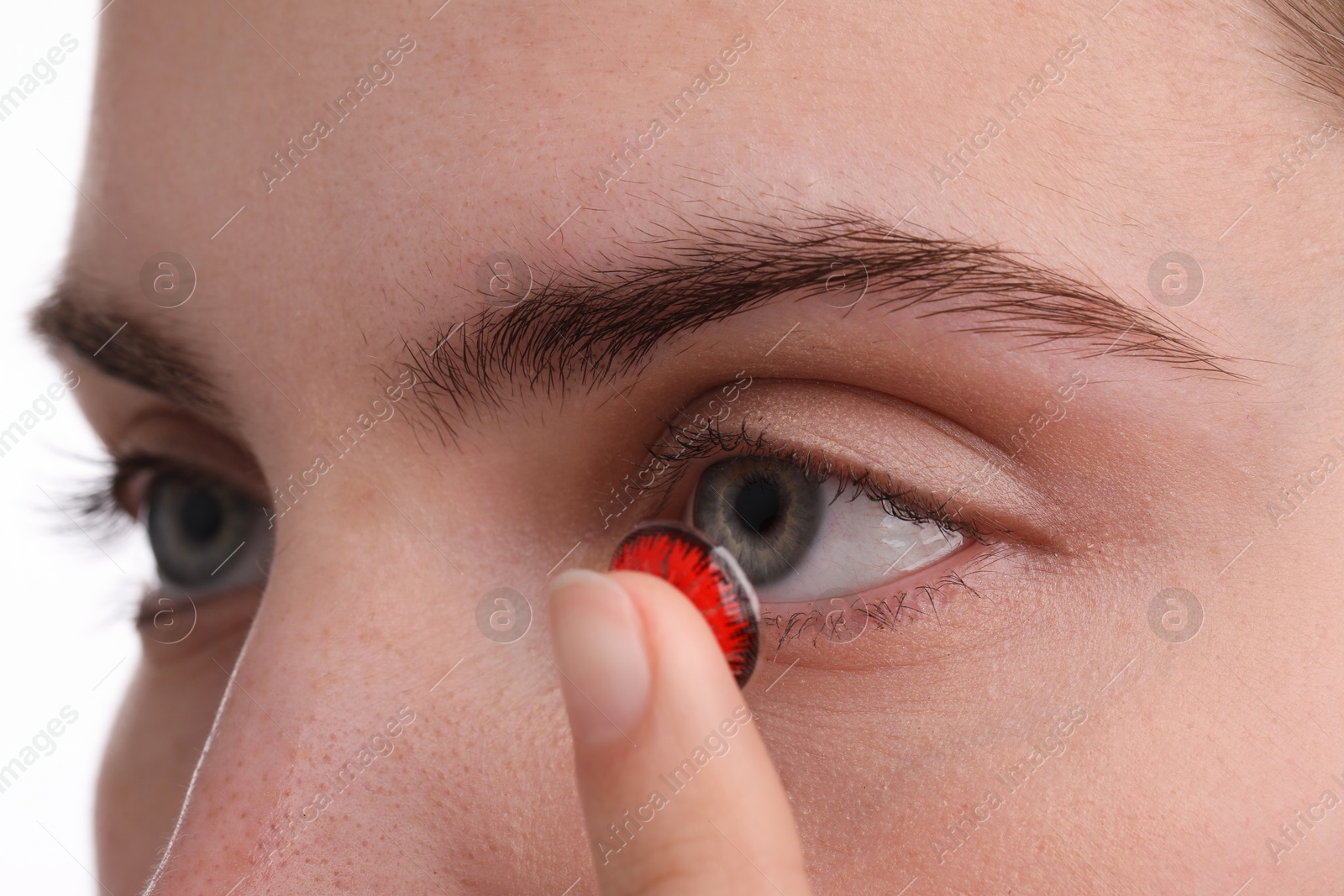 Photo of Woman putting in red color contact lens on white background, closeup