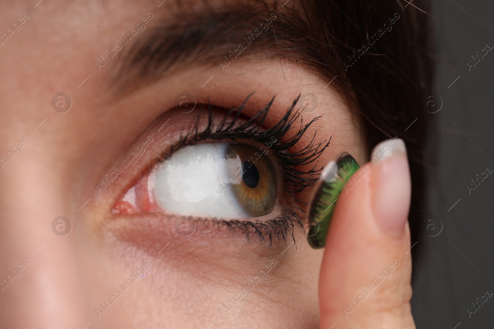 Photo of Woman putting in green color contact lens on grey background, closeup