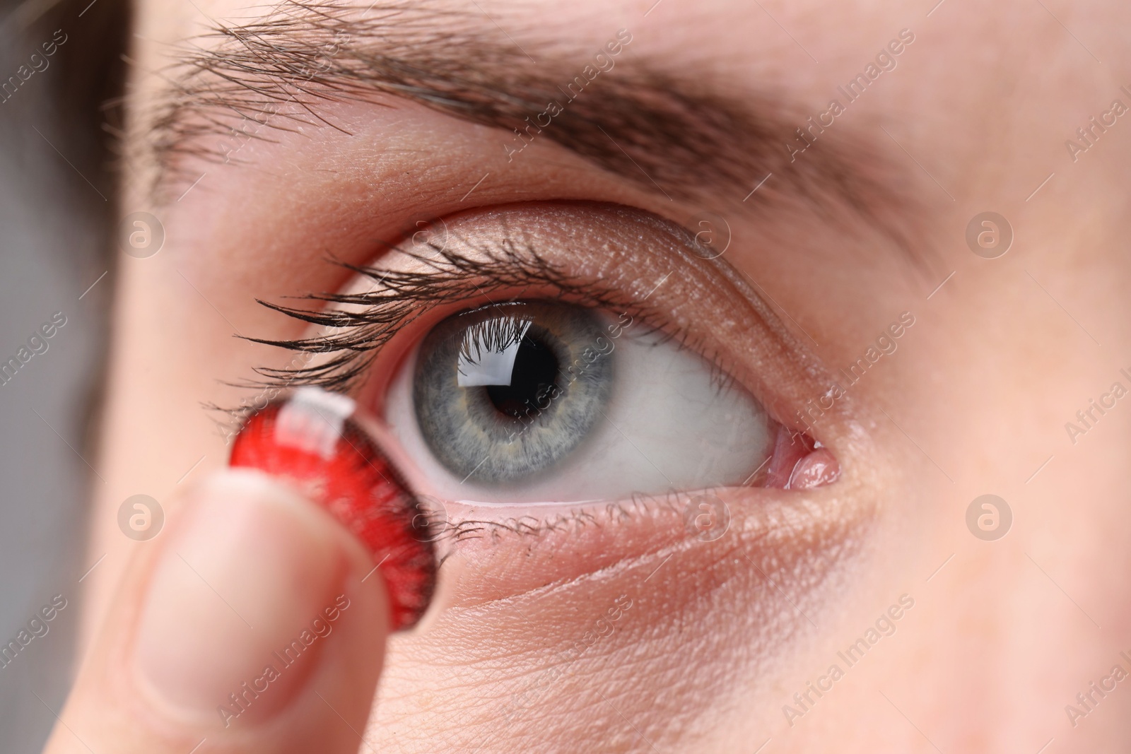 Photo of Woman putting in red color contact lens, closeup