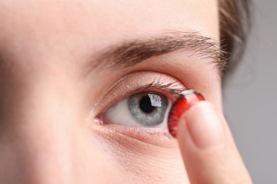 Photo of Woman putting in red color contact lens on grey background, closeup