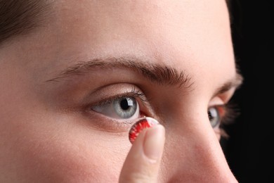 Photo of Woman putting in red color contact lens on black background, closeup