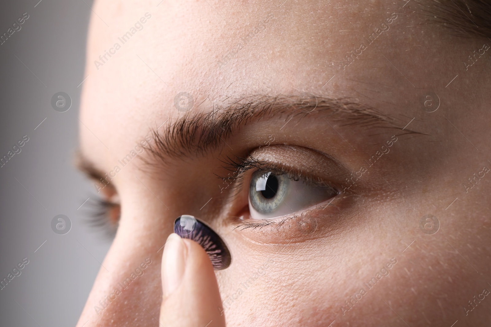 Photo of Woman putting in color contact lens on grey background, closeup