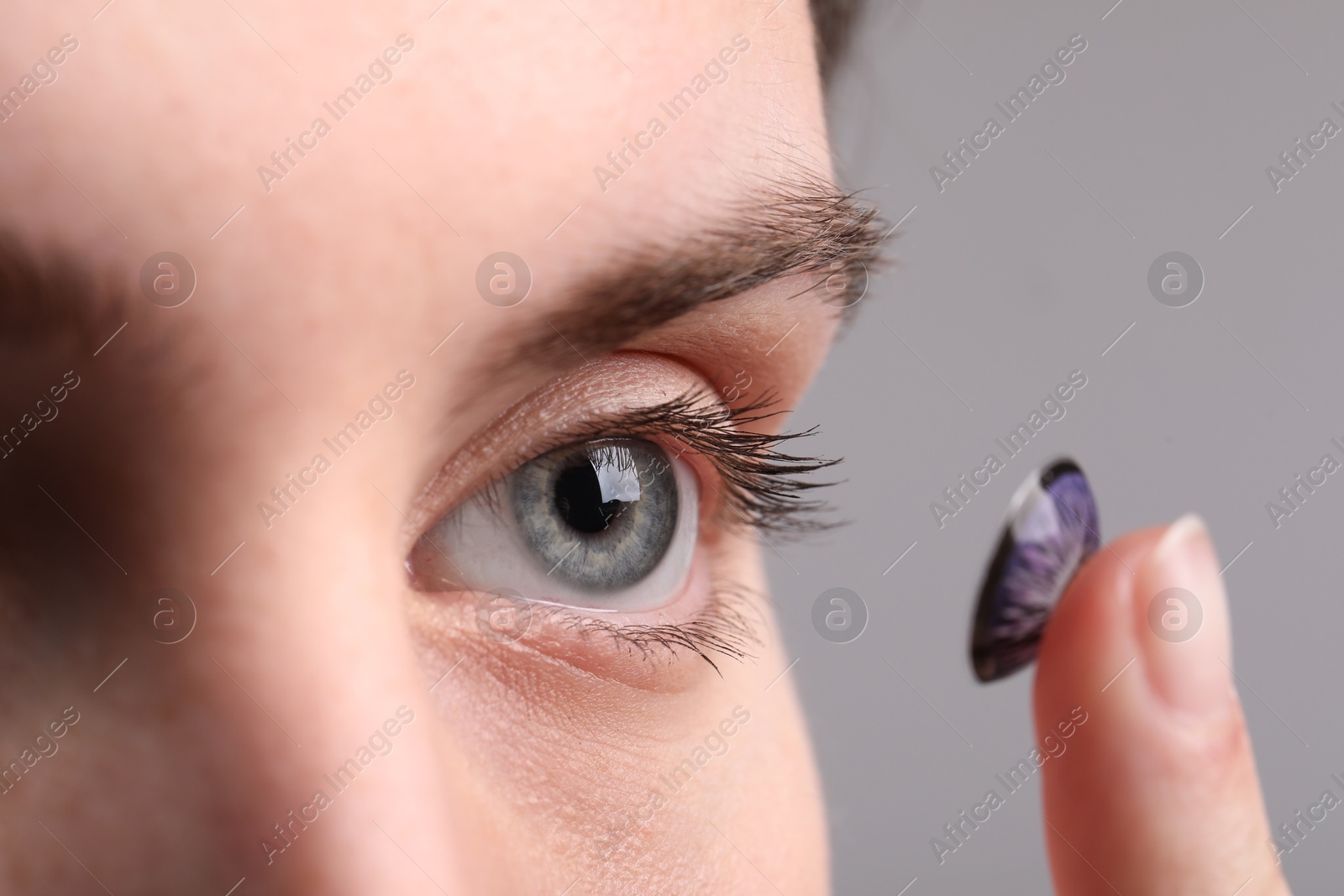 Photo of Woman putting in color contact lens on grey background, closeup