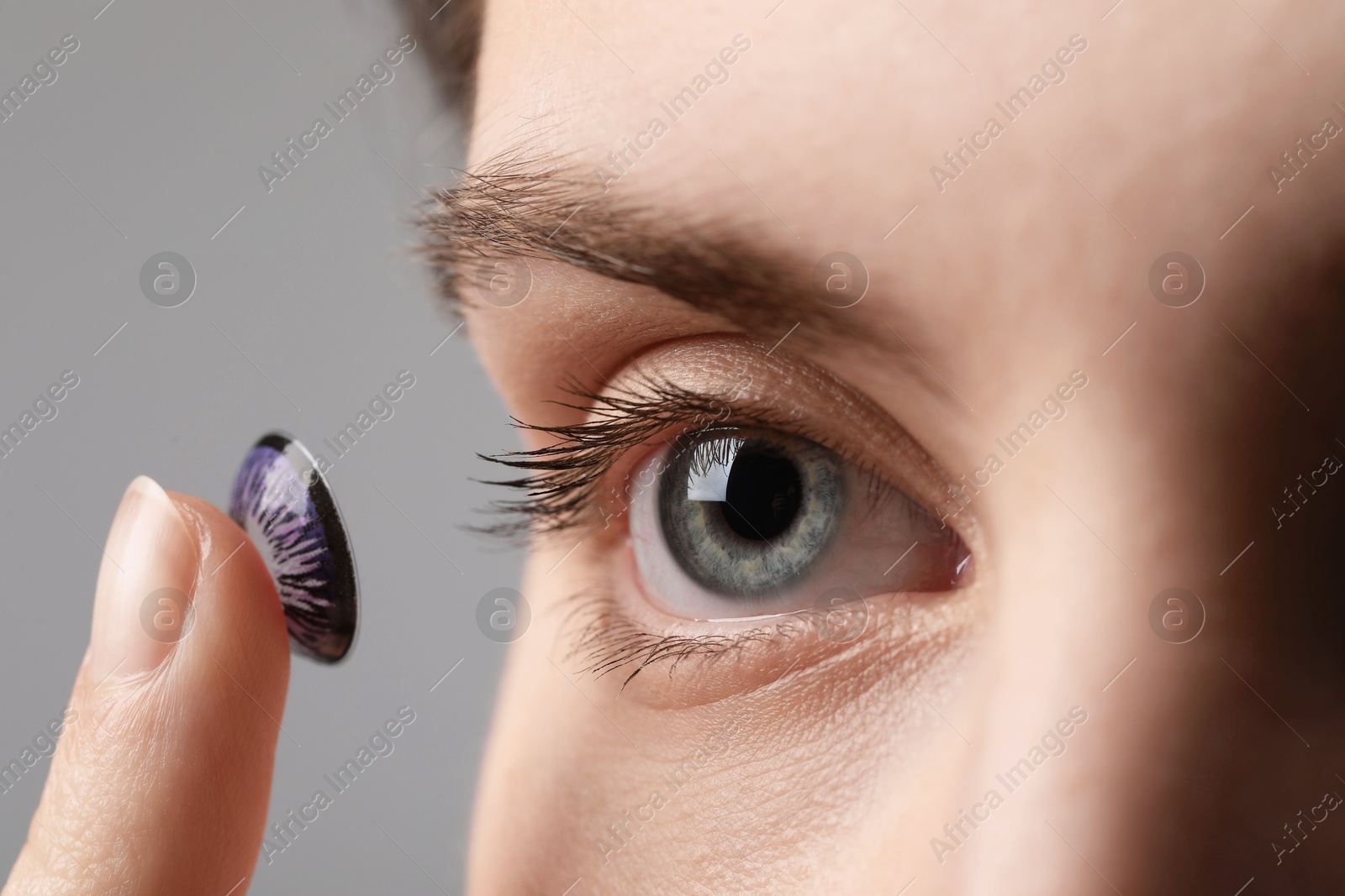 Photo of Woman putting in color contact lens on grey background, closeup