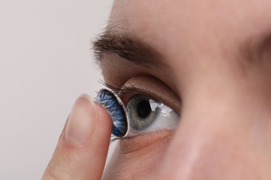 Photo of Woman putting in blue color contact lens on light background, closeup