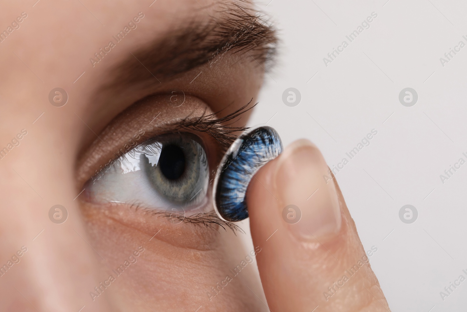 Photo of Woman putting in blue color contact lens on light background, closeup