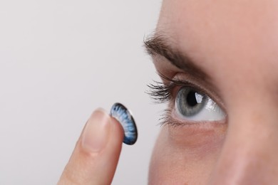 Photo of Woman putting in blue color contact lens on light background, closeup. Space for text