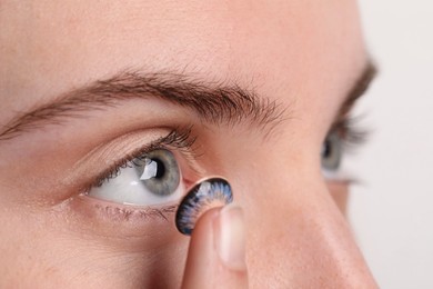 Photo of Woman putting in blue color contact lens on light background, closeup