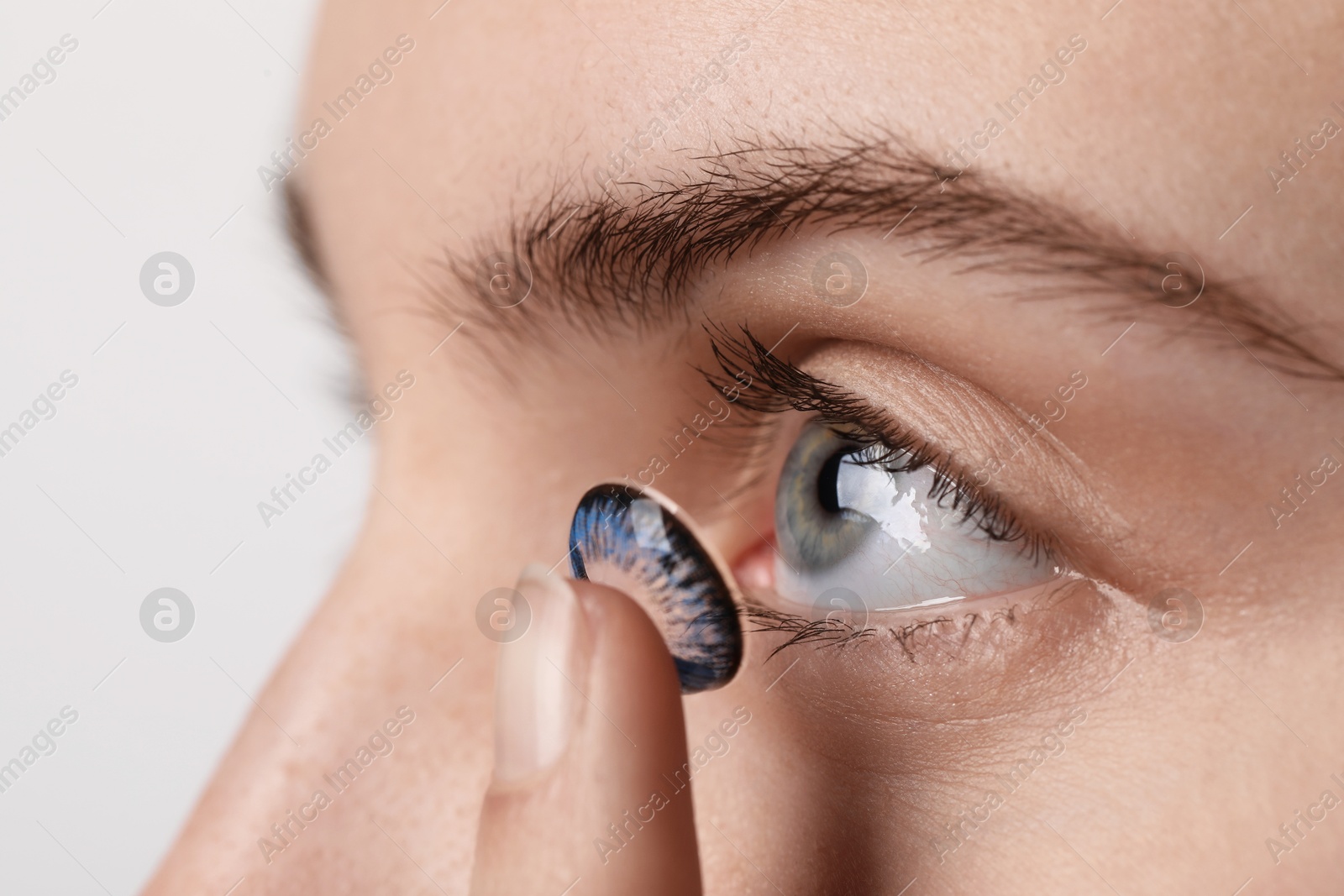 Photo of Woman putting in blue color contact lens on light background, closeup