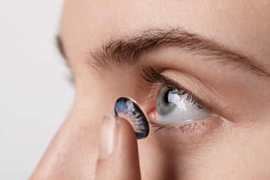 Photo of Woman putting in blue color contact lens on light background, closeup