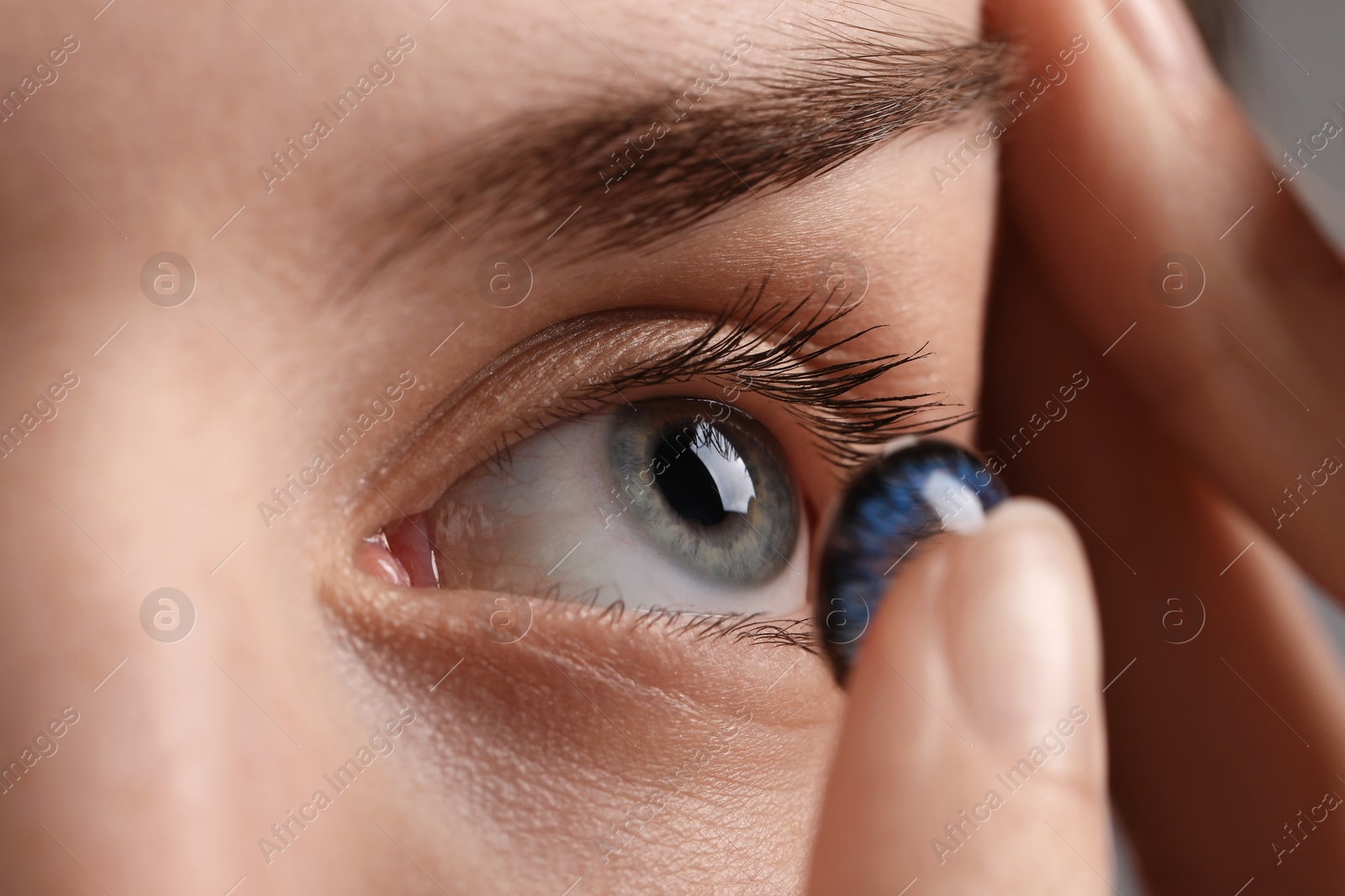 Photo of Woman putting in blue color contact lens, closeup