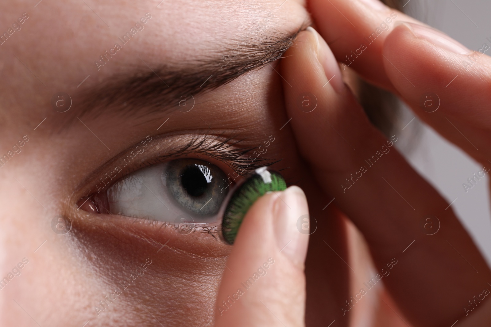 Photo of Woman putting in green color contact lens on grey background, closeup