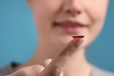 Photo of Woman with red color contact lens on light blue background, closeup. Selective focus