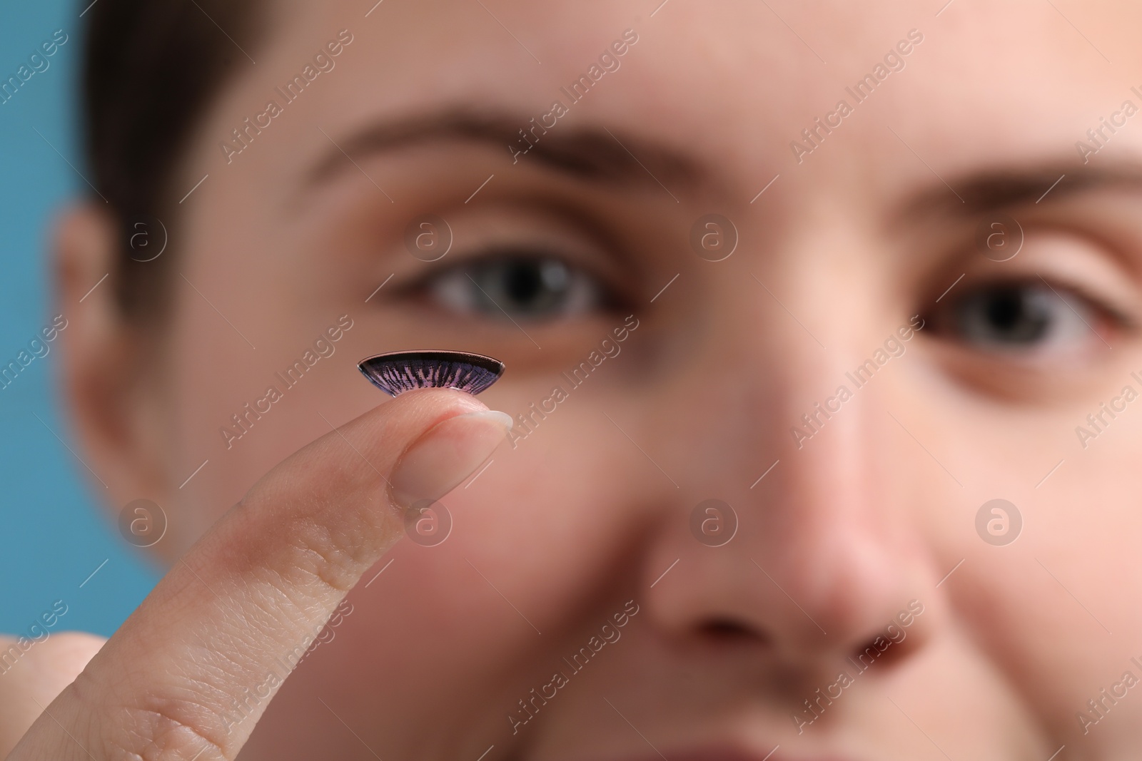 Photo of Woman with color contact lens on light blue background, closeup. Selective focus