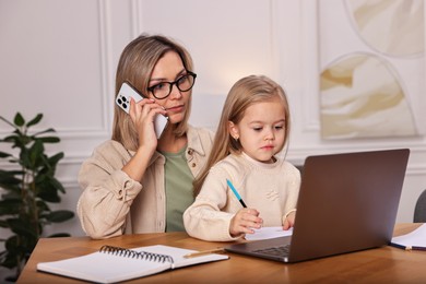 Photo of Work-family balance. Single mother talking by smartphone and her daughter drawing at wooden table indoors