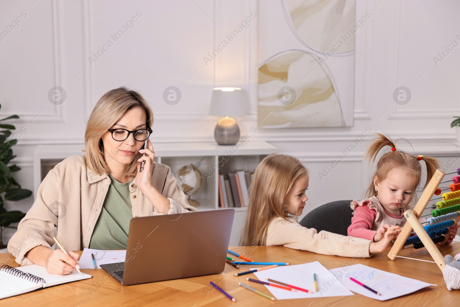 Photo of Work-family balance. Single mother talking by smartphone and her children at wooden table indoors