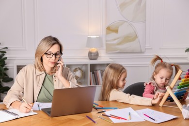 Photo of Work-family balance. Single mother talking by smartphone and her children at wooden table indoors